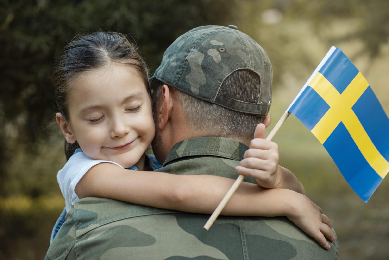 Little girl hugs the soldier father and holding Swedish flag.